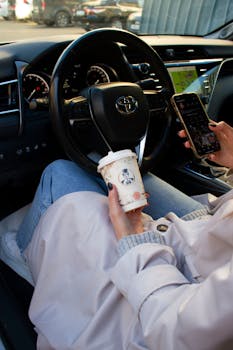 A woman holding coffee and smartphone inside a car, showcasing modern lifestyle.