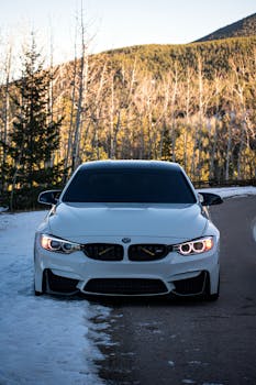 Stylish white car parked elegantly on a snowy mountain road, surrounded by winter trees.