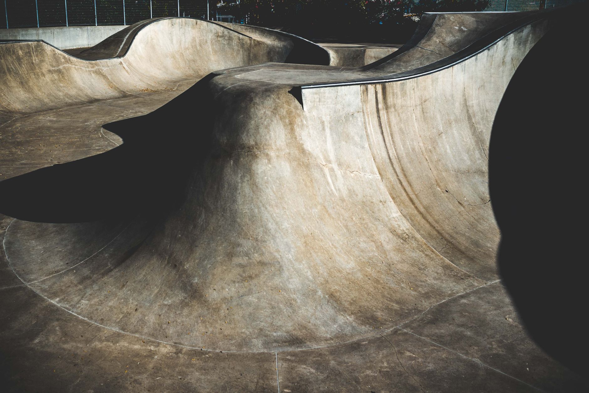 A worn concrete skate pool in Houston at sunset, with a skater grinding coping beside faded graffiti