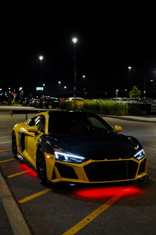 Free A sleek yellow sports car parked at night with glowing red lights underneath. Stock Photo