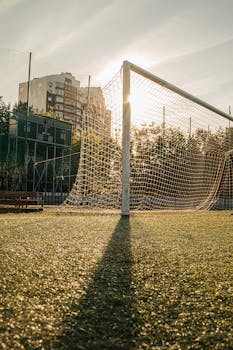 A football goal on an urban pitch during sunset with tall buildings in the background.