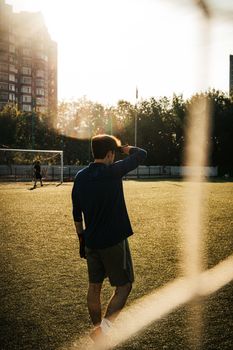 A man walks on a soccer field in sunlight, casting long shadows during the day.