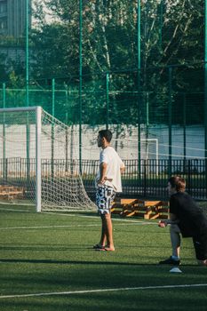 Two men engaging in a casual soccer game on a sunlit outdoor field, surrounded by green fencing.