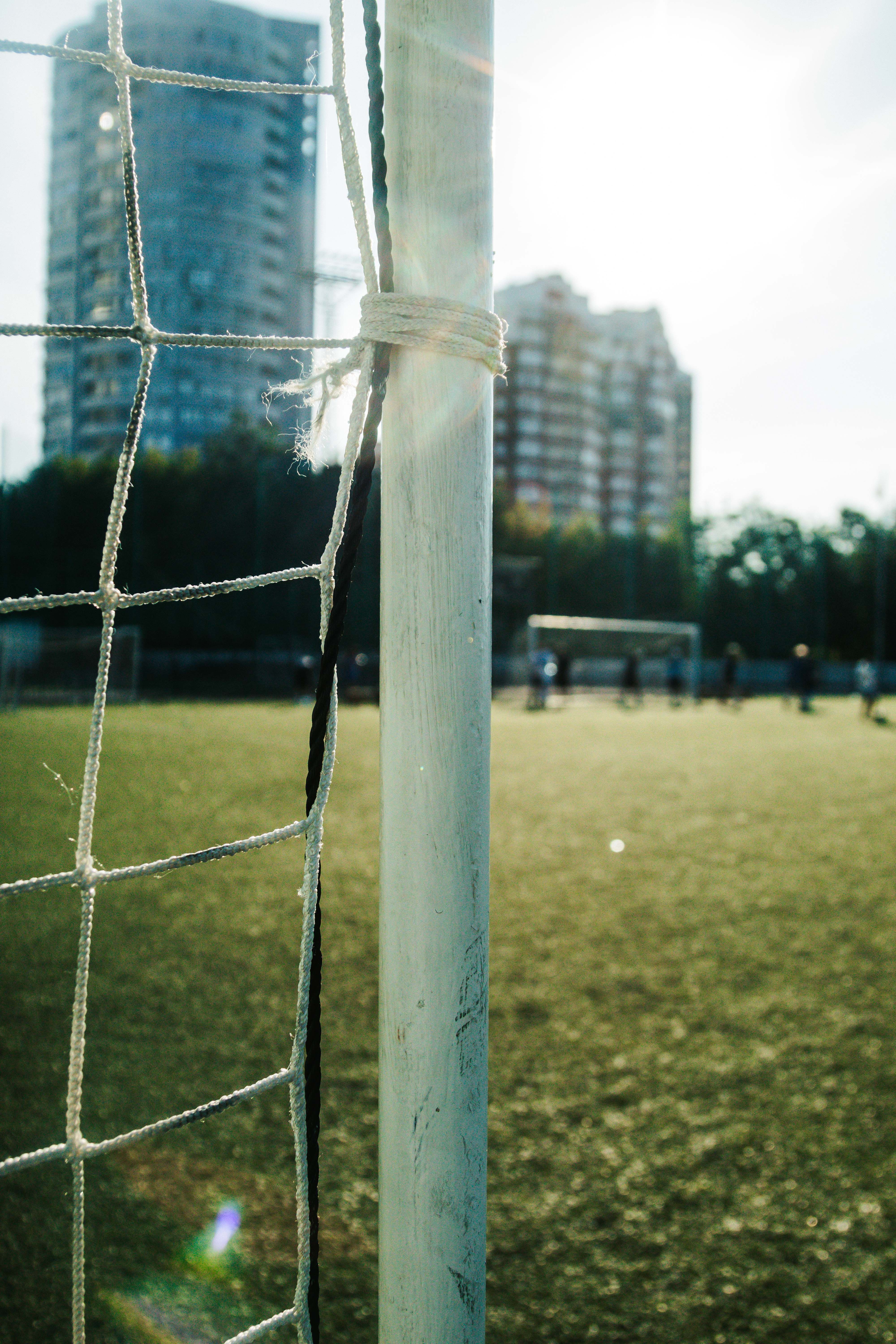 Close-up of a soccer goal with a cityscape backdrop in bright sunlight.