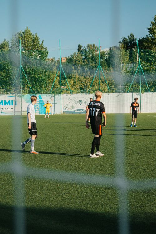 Free Soccer game on a sunny day with young men on the field, captured beyond the net. Stock Photo