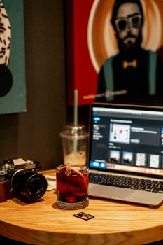 Close-up of a cozy desk setup with a drink, laptop, and vintage camera.