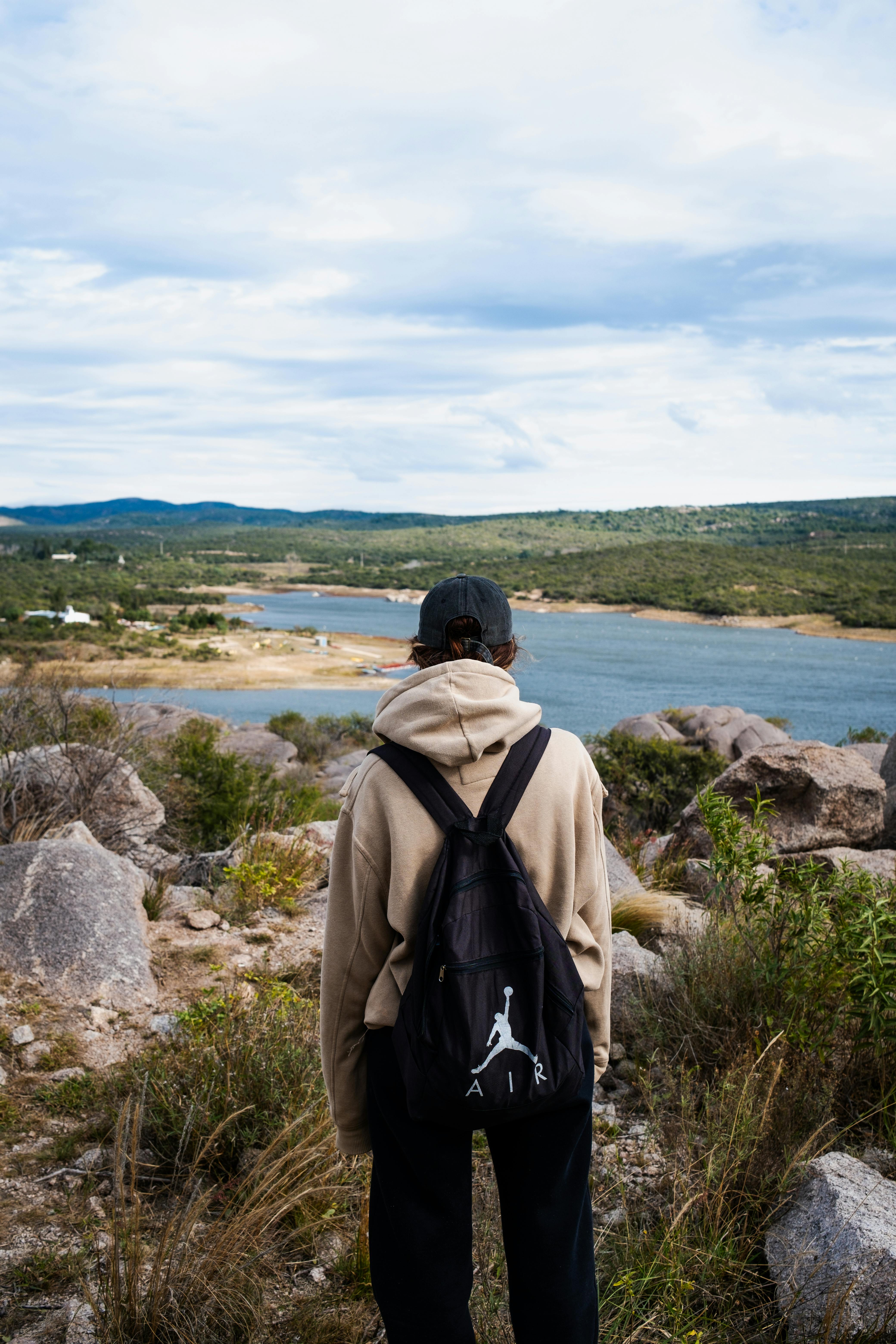 Person with backpack enjoying a scenic view of a river and landscape outdoors.