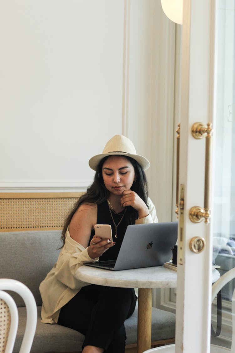 Woman In Straw Fedora Sitting In Cafe With Smartphone And Laptop