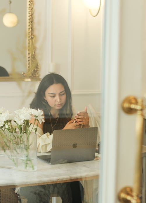 Young Woman Texting Sitting in Front of a Laptop