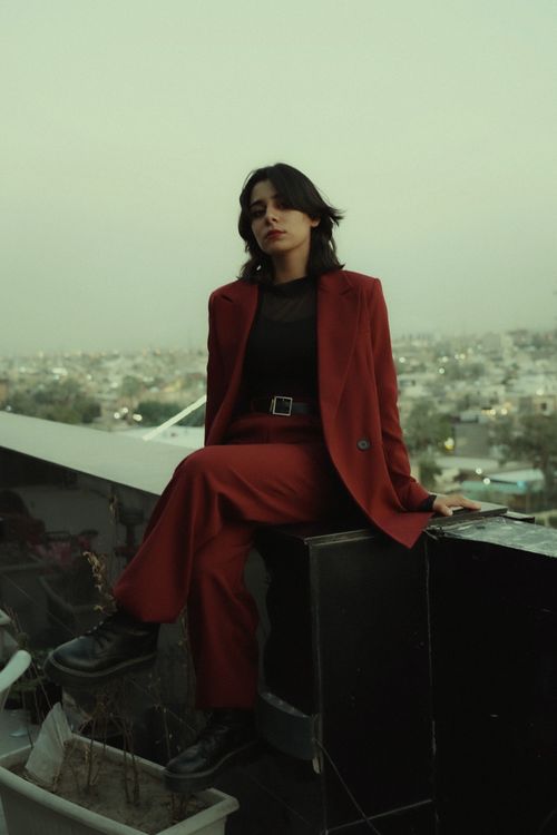 Free Fashion model in red suit posing on urban rooftop with cityscape view. Stock Photo
