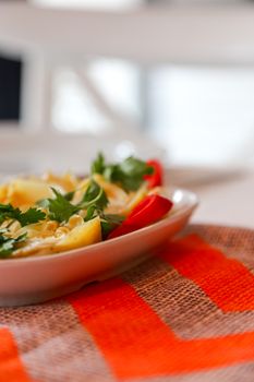 A vibrant summer salad with fresh ingredients served in a white bowl on an orange-red tablecloth.