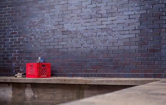 A red plastic crate sits against a dark brick wall in an empty urban setting.
