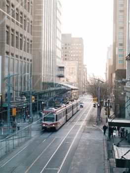 A bustling city street with a tram passing by tall office buildings, showcasing modern urban life.