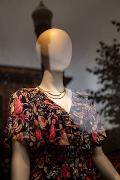 Elegant mannequin in floral dress with necklace in store window display, reflecting urban street.