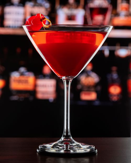 Free A classic Manhattan cocktail garnished with a maraschino cherry in a dimly lit bar setting. Stock Photo