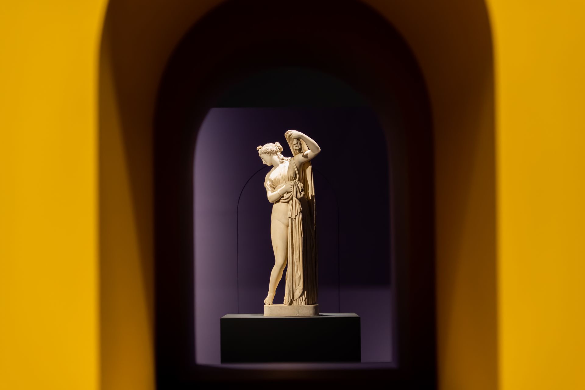 A classic marble sculpture framed by a striking yellow archway, emphasizing artistic elegance.