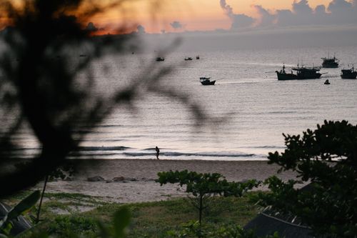 Free Tranquil beach with fishing boats and a silhouette of a person during sunset, creating a peaceful ambiance. Stock Photo