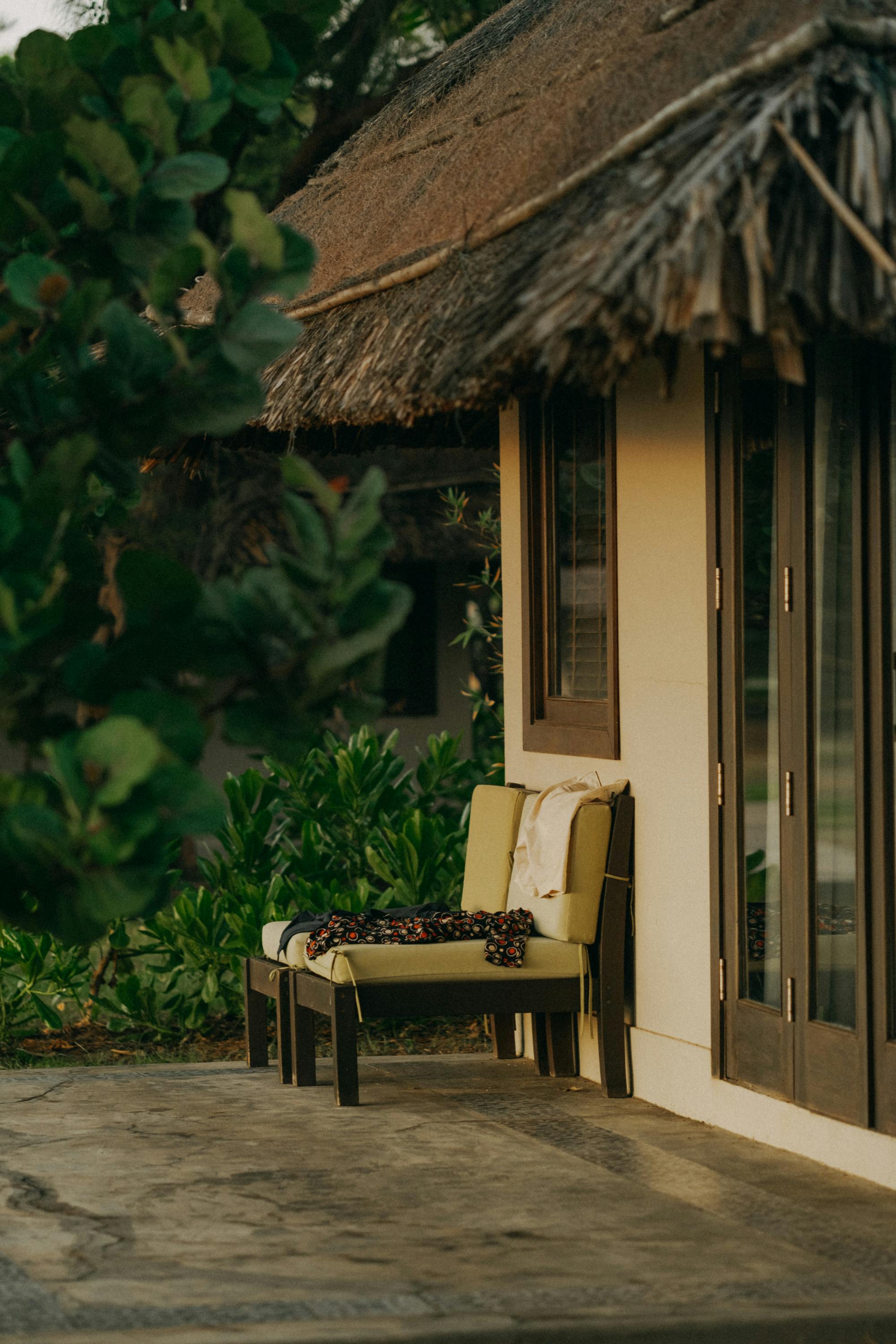 A serene image of a cottage with a thatched roof, featuring a cozy terrace with green foliage.