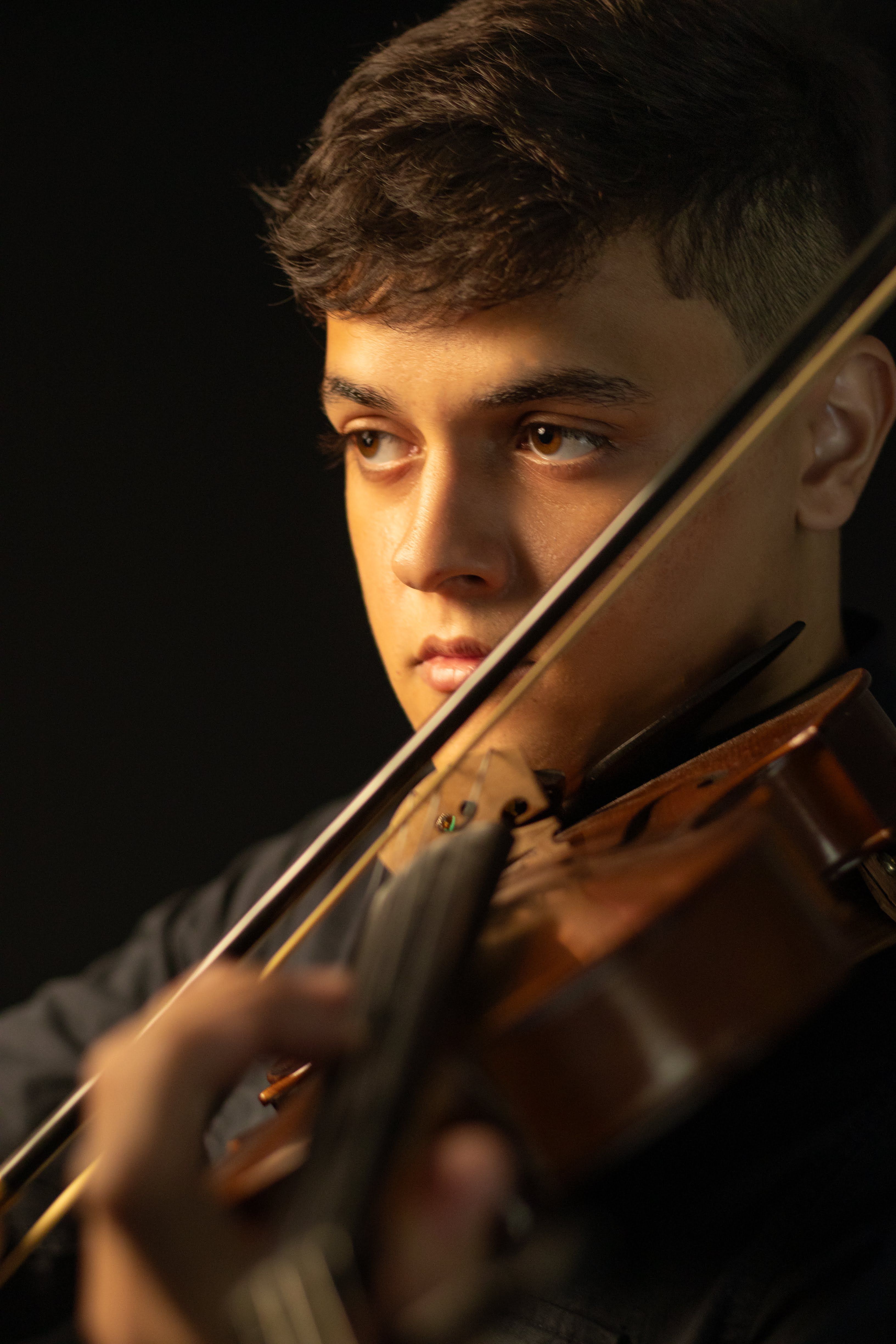 Close-up of a young man playing the violin against a black background.
