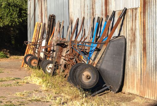 Free A collection of old wheelbarrows lined up against a rustic corrugated metal wall in a rural setting. Stock Photo
