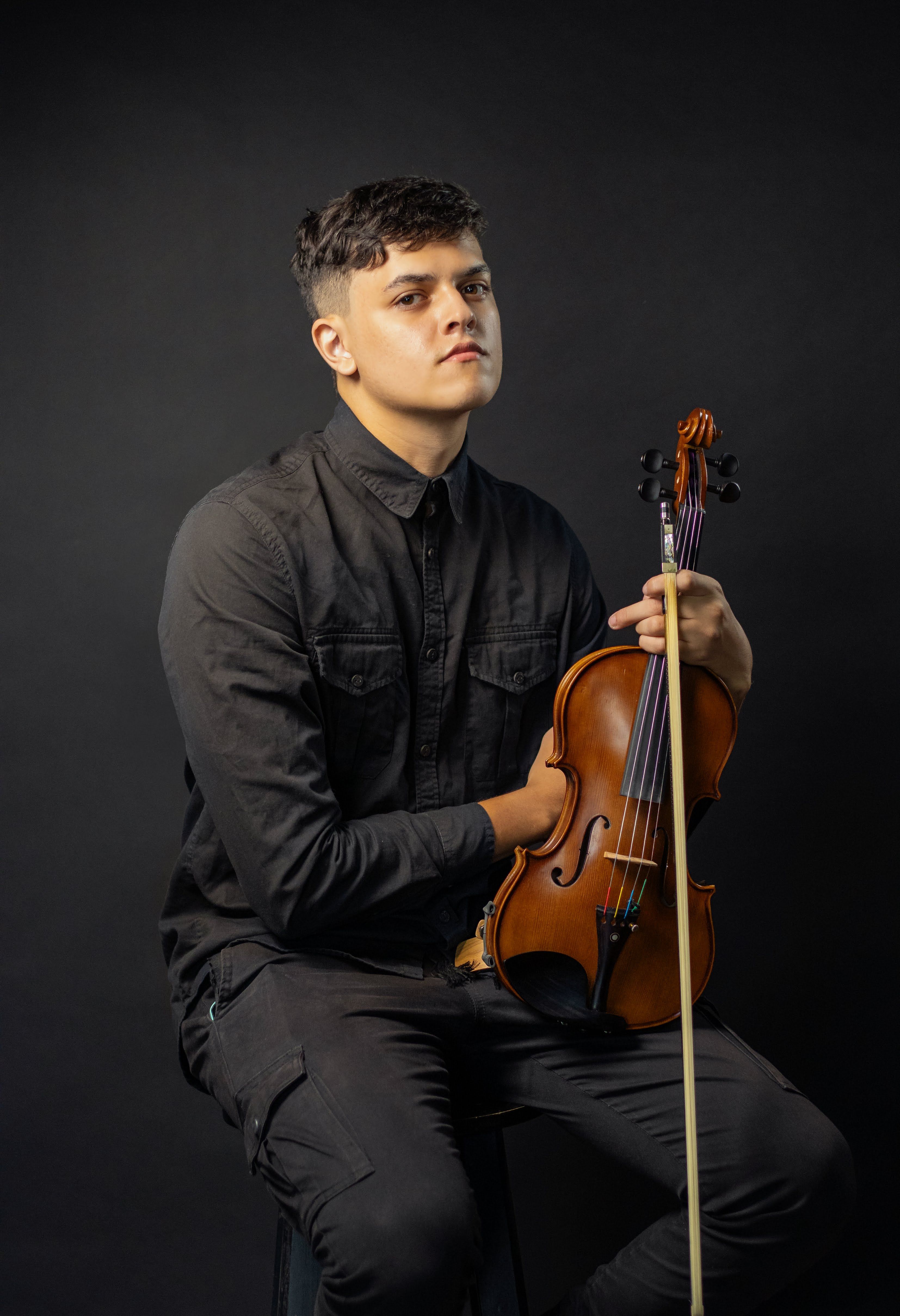 A young male violinist poses confidently in a studio setting, highlighting musical passion.
