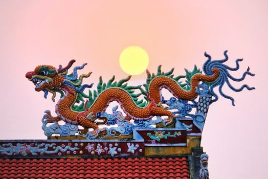 Colorful dragon decoration on a traditional Chinese roof with a pink sky at sunset.