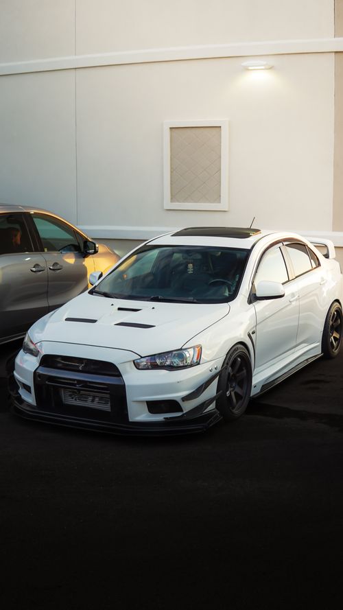 Free A white Mitsubishi Lancer Evolution parked in an urban parking area under warm lighting. Stock Photo