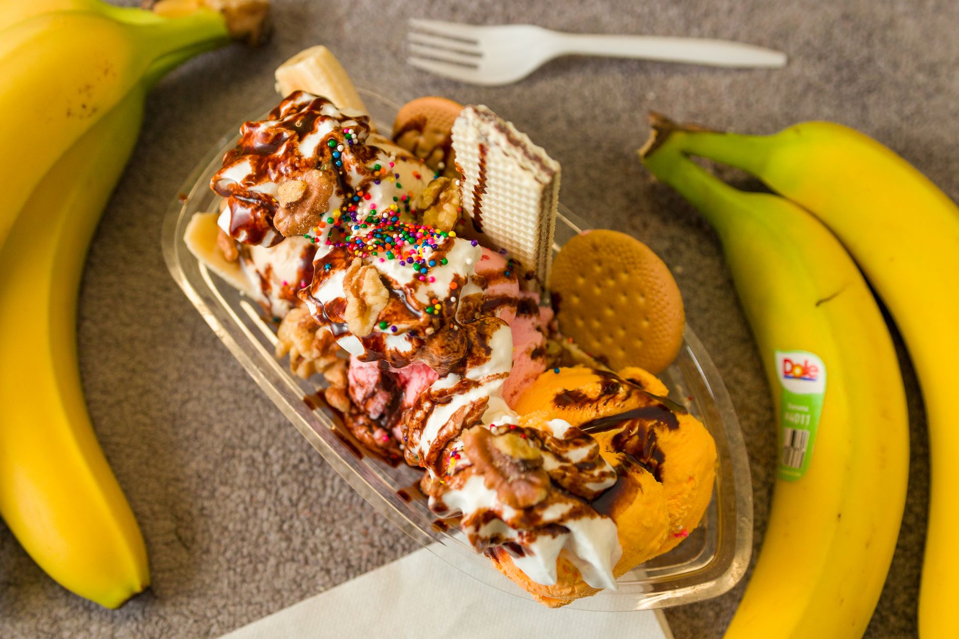 three chocolate-dipped frozen bananas on a yellow picnic table: one rolled in chopped peanuts, one c