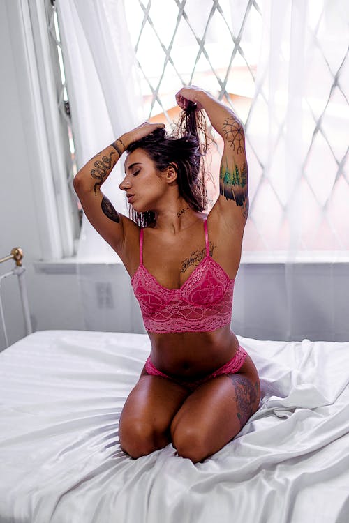 Woman Wearing Pink Lingerie Kneeling on Top of Bed While Tying Hair