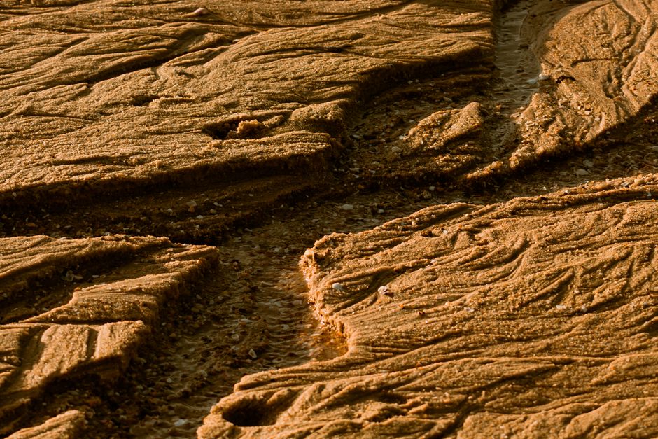 Detailed view of sunlit eroded sand patterns creating a textured and natural surface.