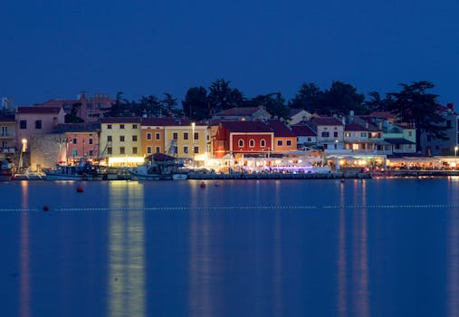 Illuminated harbor with colorful houses in Novigrad, Croatia at night, reflecting in calm water.