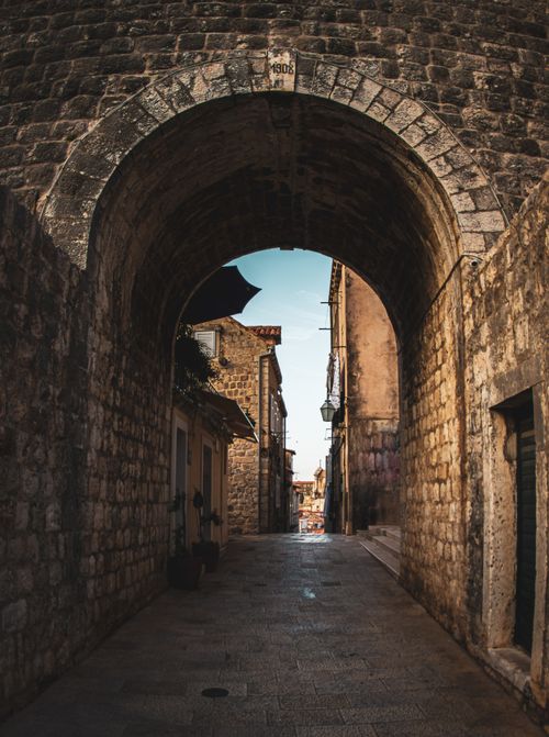 Free Discover the historic charm of Dubrovnik's cobblestone streets through a Gothic stone archway. Stock Photo