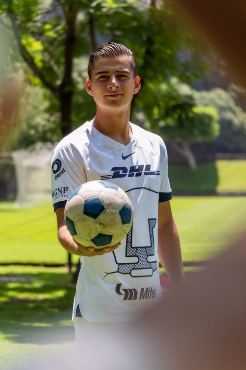 Free A young male footballer wearing a sports jersey holds a soccer ball in a sunny park. Stock Photo