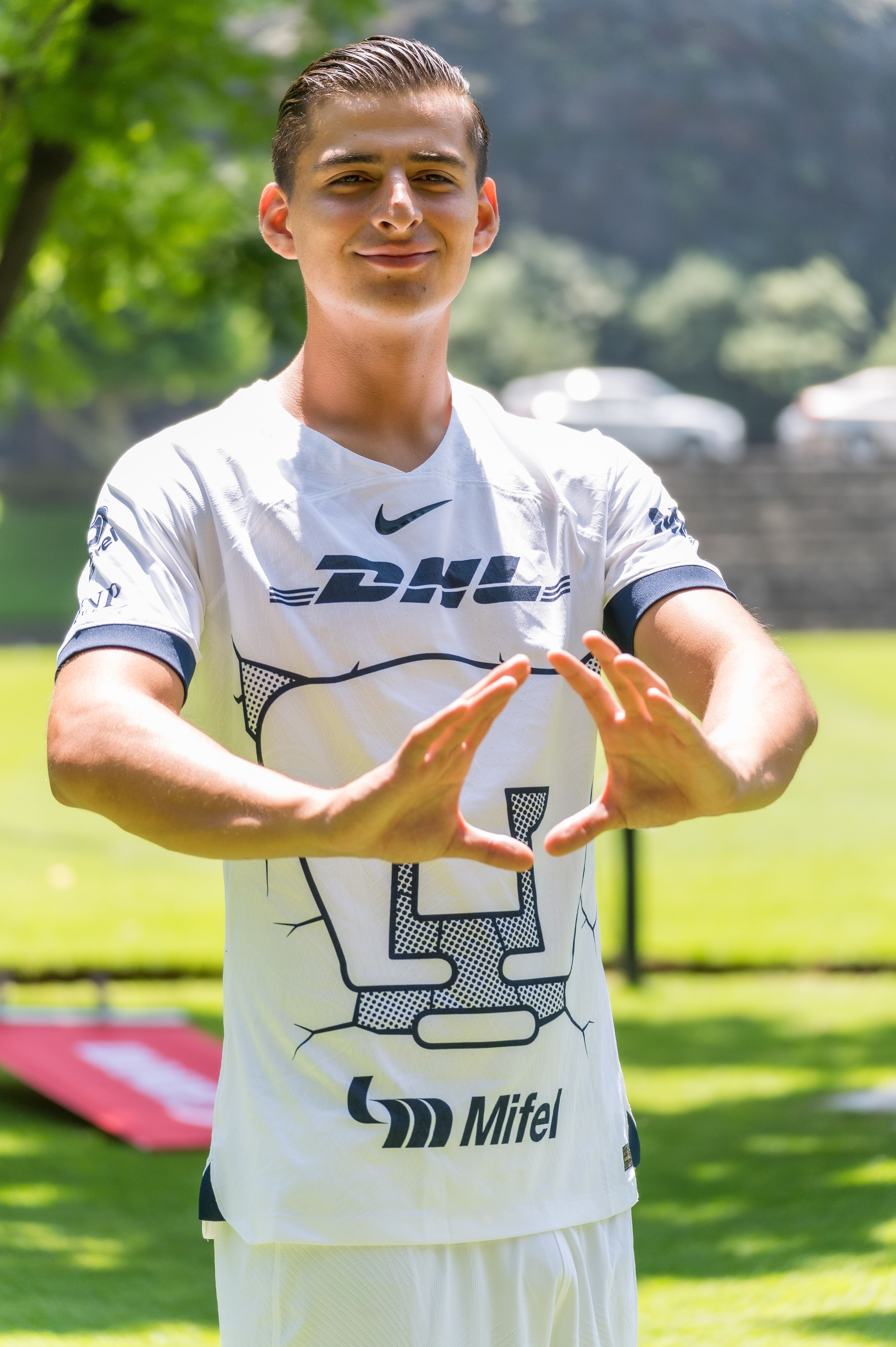 A young male football player poses confidently outdoors in a sunny setting.