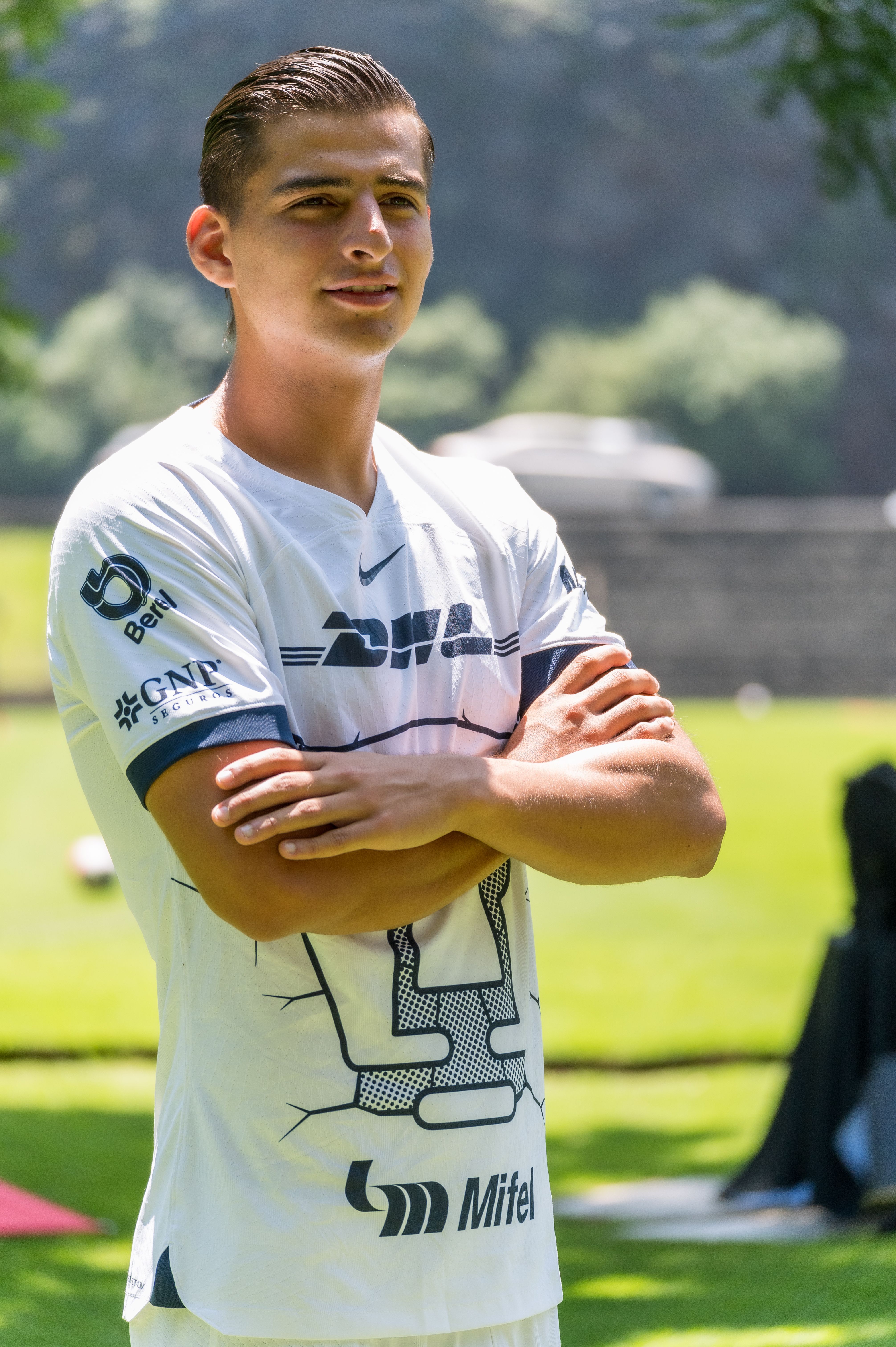 Confident young soccer player posing in a team jersey with arms crossed outdoors.