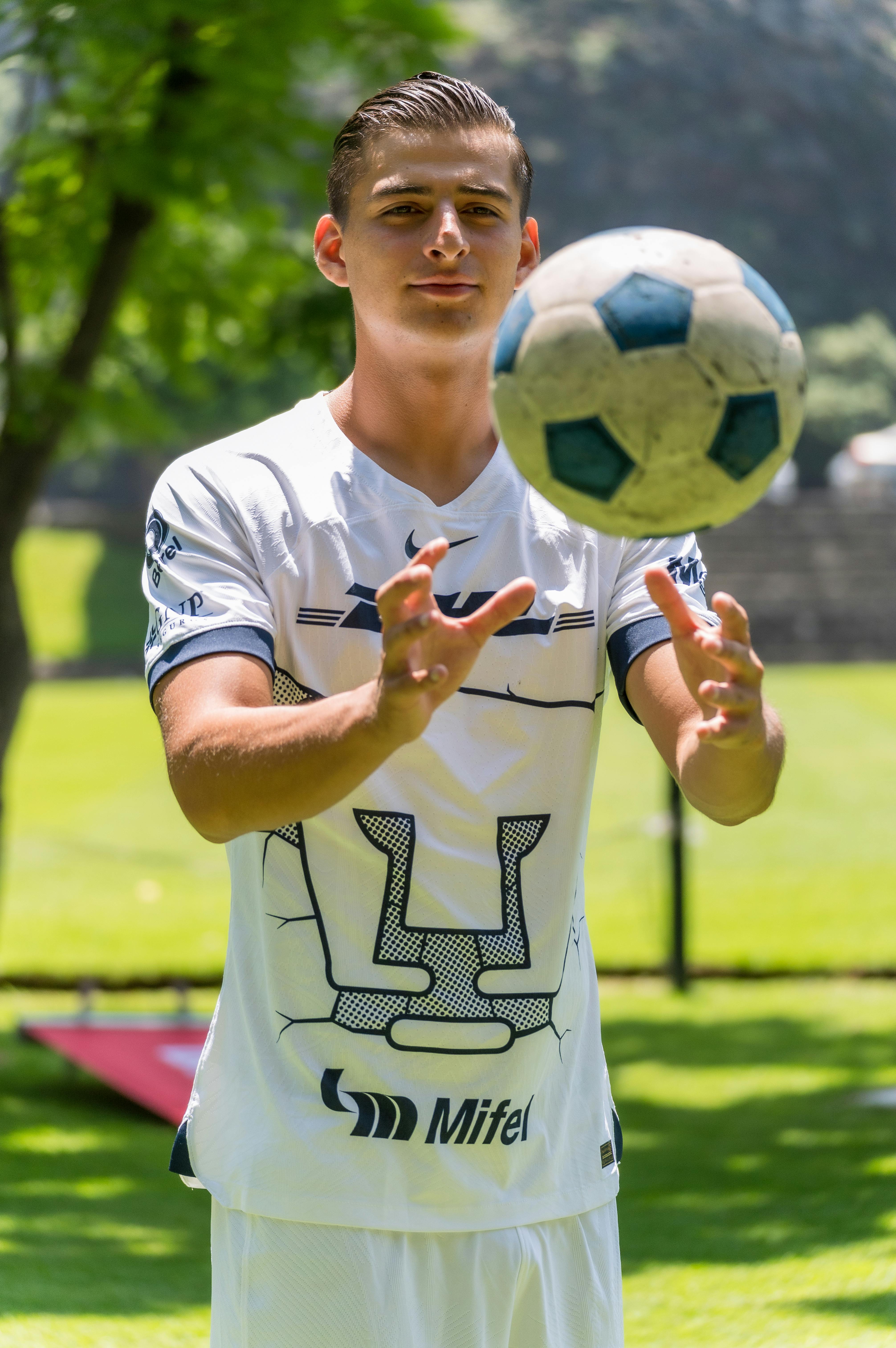 A young male soccer player in athletic gear throws a ball outdoors on a sunny day.
