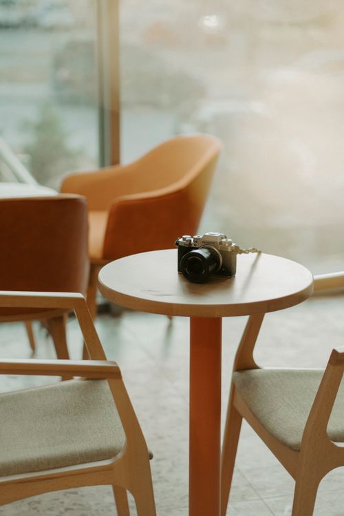 Free Warm interior scene featuring a camera on a wooden table with armchairs. Stock Photo