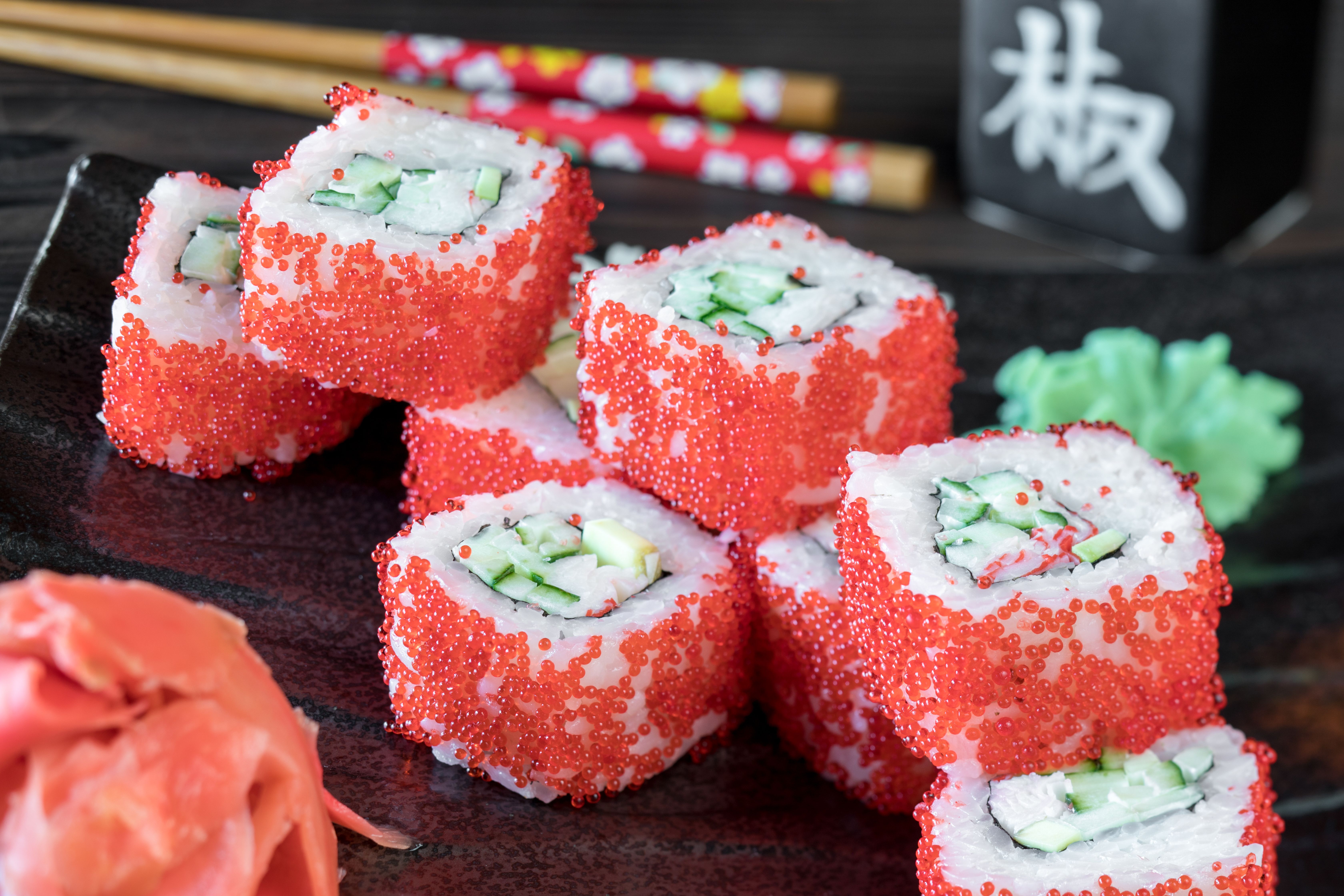 Colorful sushi rolls topped with red roe, cucumber, and crab, served on a ceramic plate.