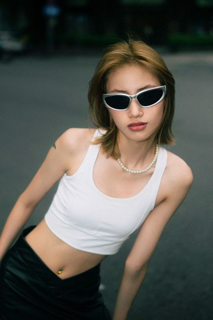 Fashionable woman in white tank top posing outdoors with sunglasses.