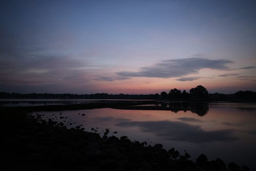 A tranquil sunset reflecting on a calm water surface, creating a peaceful rural landscape.