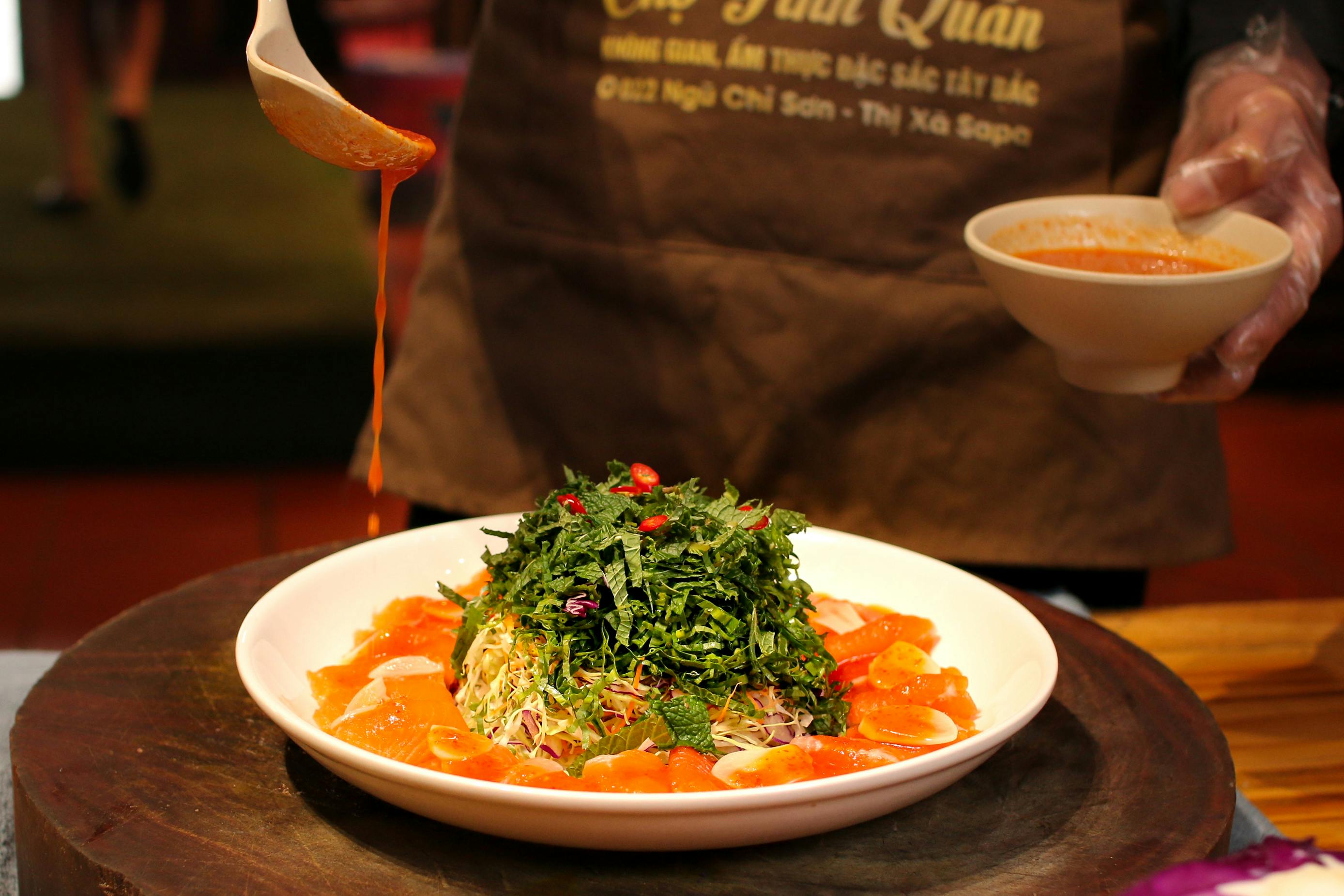 A chef drizzles vibrant orange sauce over a fresh salad on a white plate.