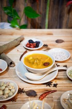Appetizing pumpkin stew in a white bowl surrounded by spices on a wooden table.