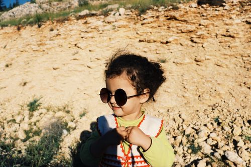 Free Adorable child with sunglasses in a sunlit rocky outdoor setting. Stock Photo