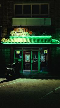 A green-lit restaurant entrance with an ornate facade in an urban setting captured at night.