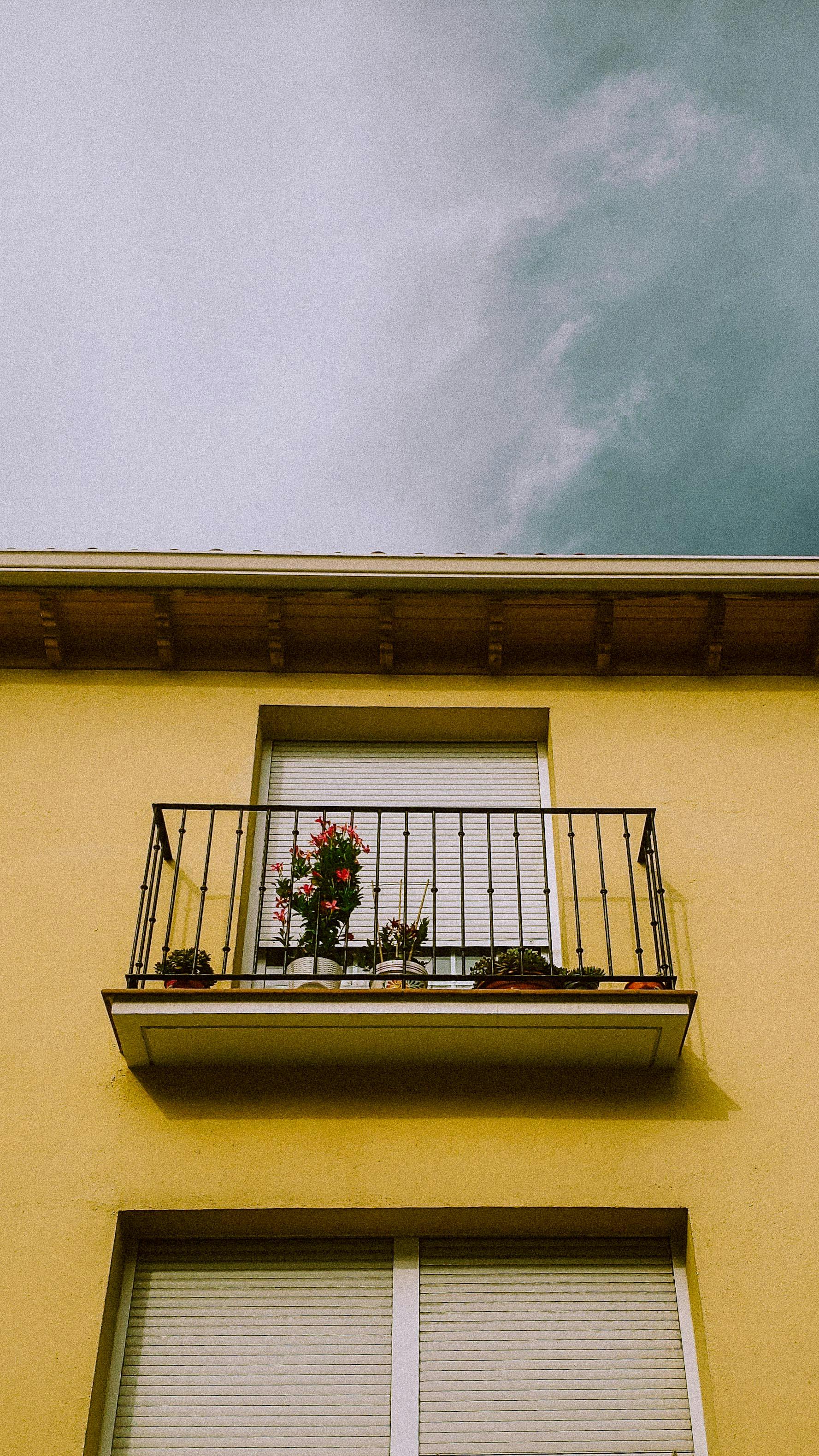 A picturesque view of a balcony with potted plants on a yellow facade in Madrid, Spain.