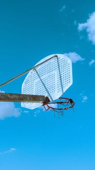 Rustic basketball hoop set against a vibrant blue sky with clouds in Madrid, Spain.