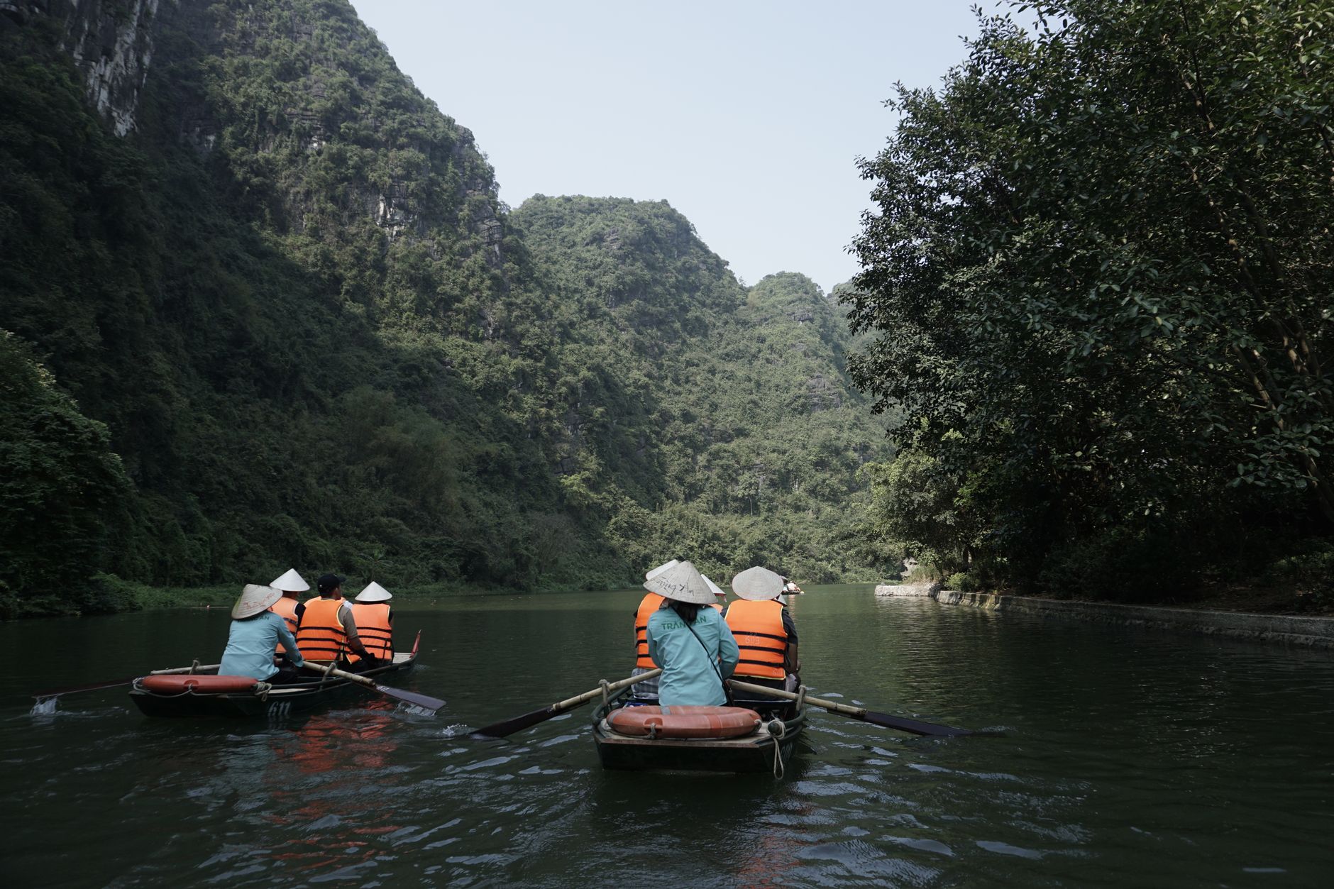 Des touristes dans des barques à rames sur une rivière paisible à Ninh Binh, au Vietnam, entourés de montagnes verdoyantes.