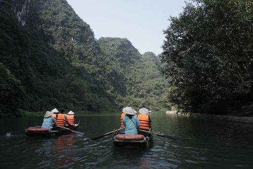 Free Tourists in rowboats on a serene river in Ninh Bình, Vietnam, surrounded by lush green mountains. Stock Photo