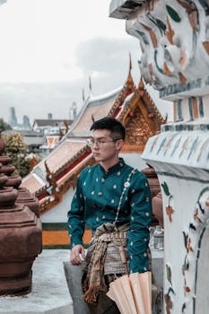 Man in traditional Thai attire at a Buddhist temple with detailed architecture.