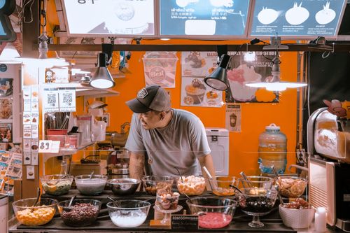 Free A man serving toppings at a vibrant street food booth indoors. Perfect for lifestyle and culinary themes. Stock Photo